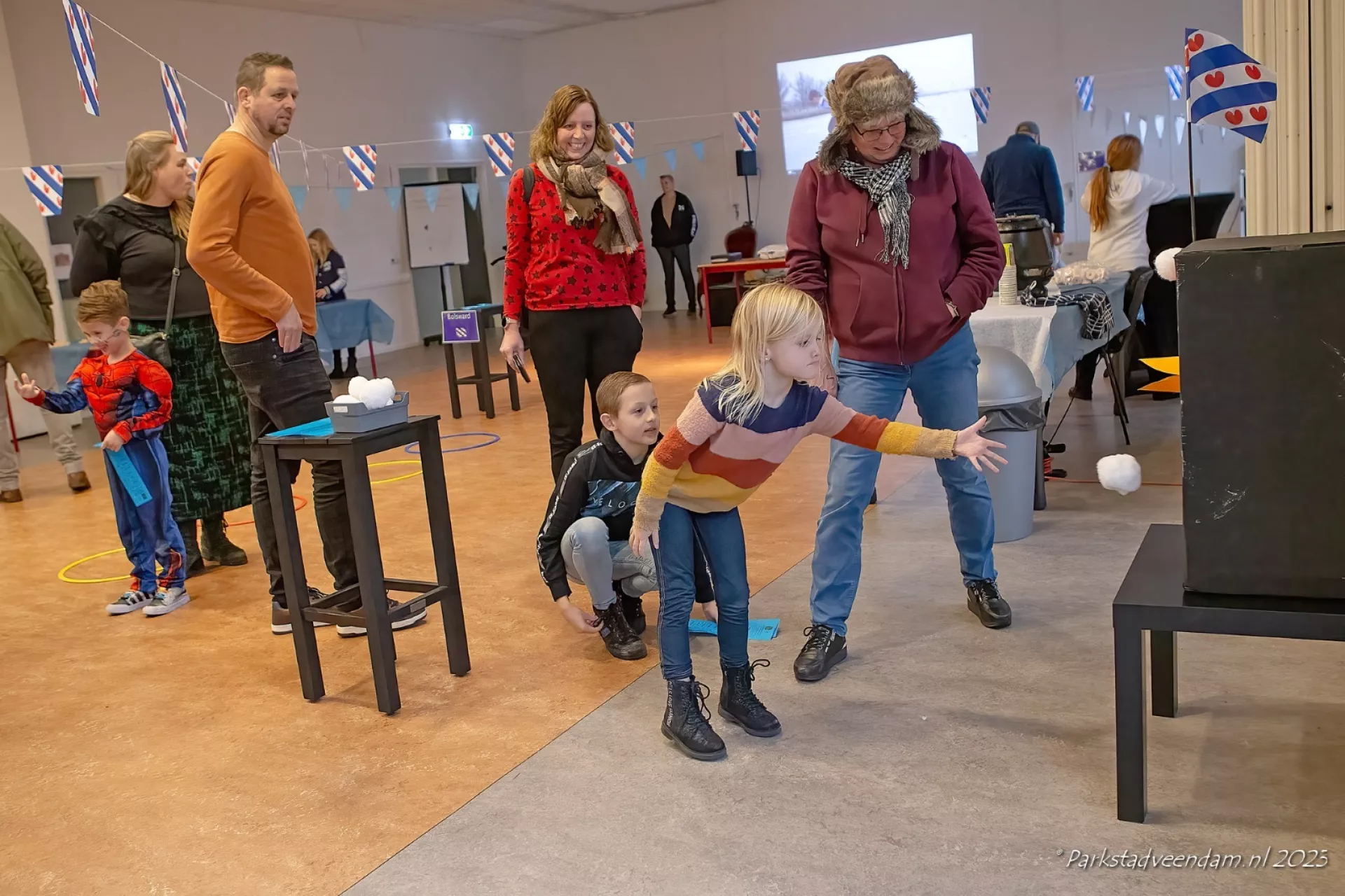 Een groep volwassenen en kinderen die binnen een spelletje spelen, ze gooien een nep sneeuwbal in een bak. Dit was onderdeel van de Elfstedenbijeenkomst van Summerfun.